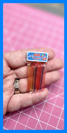 a person is holding some small pins in their hand on a pink surface with white squares