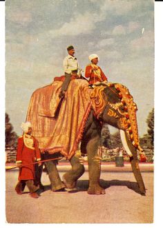 two men riding on the back of an elephant while another man stands next to it