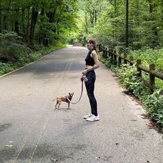 a woman is walking her dog on a leash down the road in the woods,