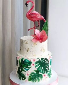 a three tiered cake decorated with pink flamingos and tropical leaves on a white table