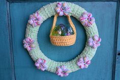 a crocheted wreath hanging on the front door with flowers and rocks in it