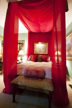 a red canopy bed in a bedroom with paintings on the wall