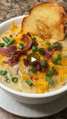 a bowl of soup with bacon, cheese and green onions next to a piece of bread