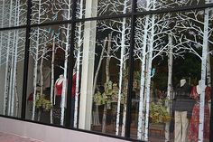 the reflection of people walking past a store window with white trees in front of it