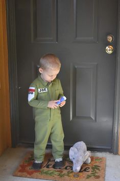 a young boy in uniform standing next to a stuffed animal and looking at a cell phone