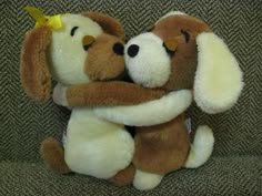 two brown and white stuffed dogs hugging each other on a couch with their eyes closed