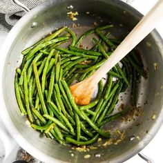 green beans being cooked in a pan with wooden spoon