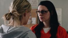 a woman with glasses talking to another woman in an orange shirt and grey sweatshirt,