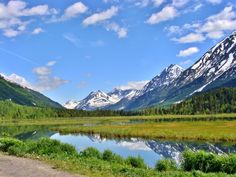 the mountains are covered in snow and green grass near a small lake with water running through it