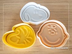 three cookie molds in the shape of hearts with faces on them, sitting on a wooden surface