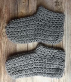 two gray crocheted mittens sitting on top of a wooden floor next to each other