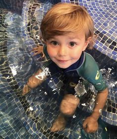 a young boy is in the water with his wetsuit on and smiling at the camera