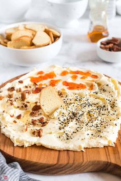 a wooden plate topped with mashed potatoes and toppings next to bowls of crackers