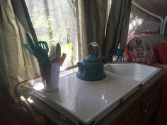 a tea kettle sitting on top of a kitchen counter next to a window with curtains