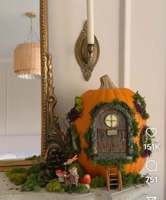 a pumpkin sitting on top of a table next to a mirror and candle holder with a fairy house in it