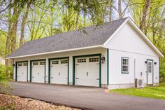 a white garage with green trim and two doors on the side of it, surrounded by trees