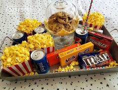 a tray filled with popcorn and snacks on top of a white tablecloth covered table