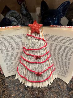 an open book with a christmas tree made out of strips of paper and red ribbon