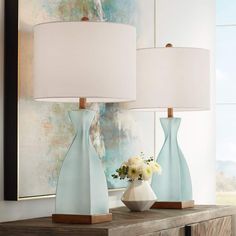 two blue vases with white flowers sit on a dresser in front of a painting