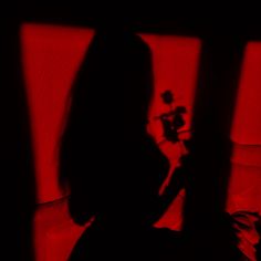 the silhouette of a woman sitting in front of a red light