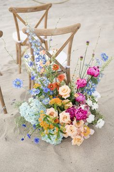 an arrangement of flowers sits on the sand next to two chairs