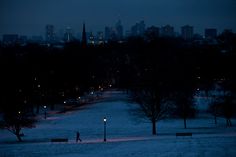 a person walking in the snow at night with city lights behind them and trees on either side