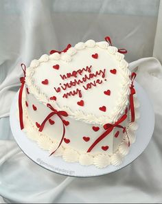 a heart - shaped cake with red ribbon and happy birthday written on it is sitting on a white plate