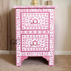 a pink and white painted chest of drawers on carpeted floor next to vases