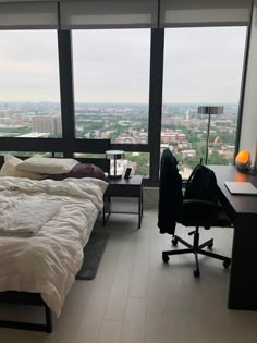 a bedroom with a bed, desk and large window overlooking cityscape in the distance