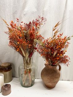 two vases with dried flowers in them on a table