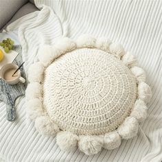 a white round pom pom sitting on top of a bed next to fruit