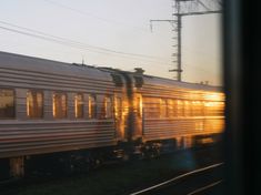 a train traveling down tracks with the sun shining on it's side and power lines in the background