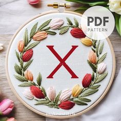 an embroidery pattern with the letter x surrounded by flowers and leaves on a wooden surface