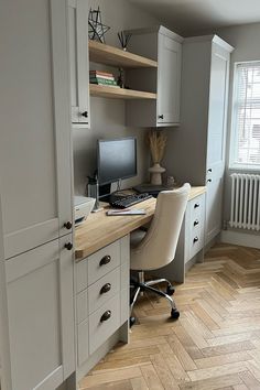 a desk with a computer on top of it next to a book shelf and cupboards