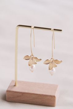 small gold flower and pearl earrings on a wooden stand