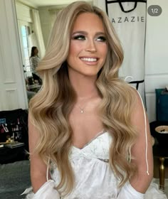 a woman with long blonde hair wearing a white dress and sitting in front of a mirror