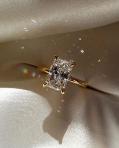 a diamond ring sitting on top of a white cloth covered in light shining from the sun