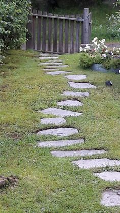 a stone path in the grass leading to a wooden fence