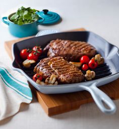 steaks and vegetables are cooking in a skillet on a cutting board next to a bowl