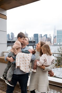 a man and woman holding two children on top of a building with the city in the background