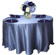 a blue table cloth with purple and white flowers in a vase on the center piece