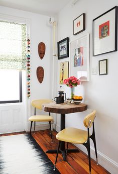 two yellow chairs sitting at a small table in front of pictures on the wall behind them