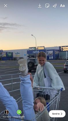 two women pushing a shopping cart in an empty parking lot, one is holding her head