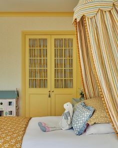 there is a bed with yellow curtains and pillows on the headboard, next to a doll house