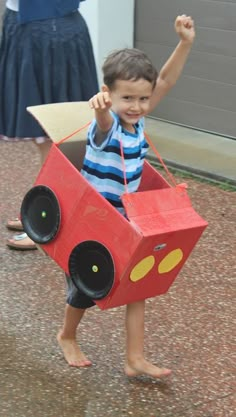 a young boy is holding up a cardboard box shaped like a race car with wheels