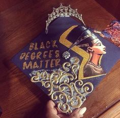 a black queen's matter graduation cap is being held by a person wearing a tiara