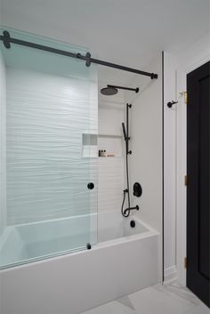 a bathroom with a tub, shower head and black handles on the door knobs