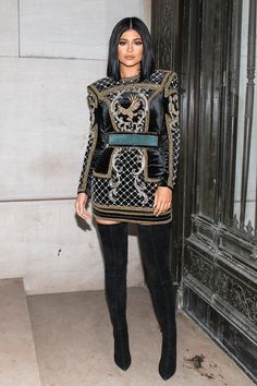 a woman in black and gold outfit standing next to a door with her hand on her hip