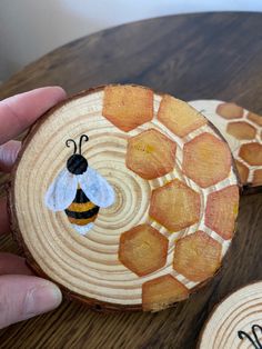 a hand holding a piece of wood with a bee painted on it