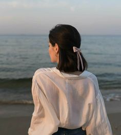 a woman standing on top of a beach next to the ocean wearing a white shirt